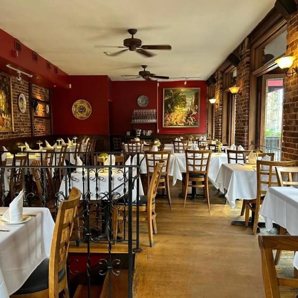 The Bacco Ristorante & Bar dining room features red walls, brick, white tablecloths, and wooden chairs.