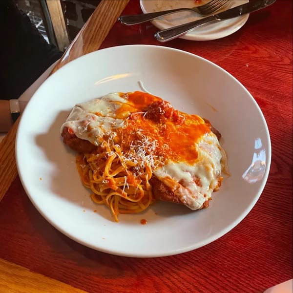 Chicken parmesan with spaghetti and red sauce, topped with melted cheese and grated parmesan.