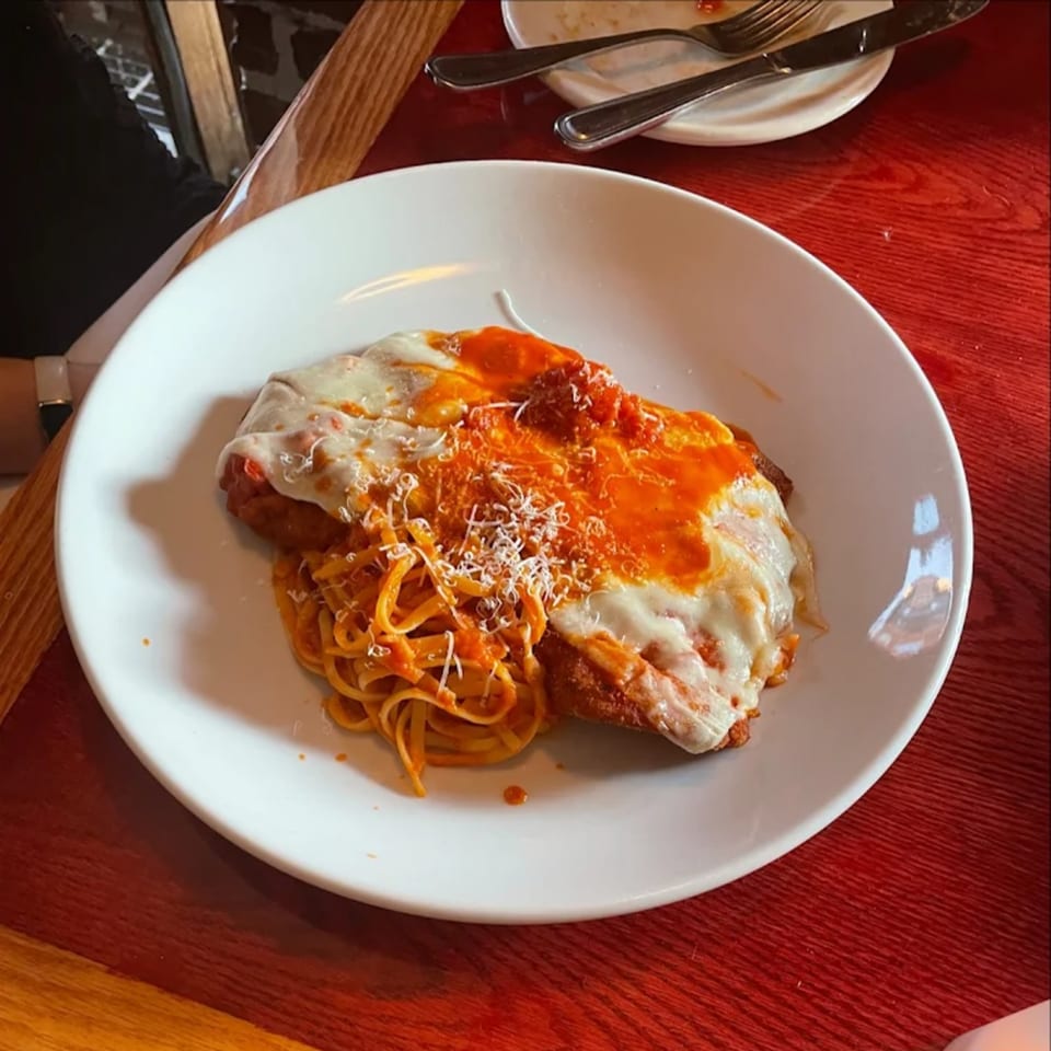 Chicken parmesan with spaghetti and red sauce, topped with melted cheese and grated parmesan.