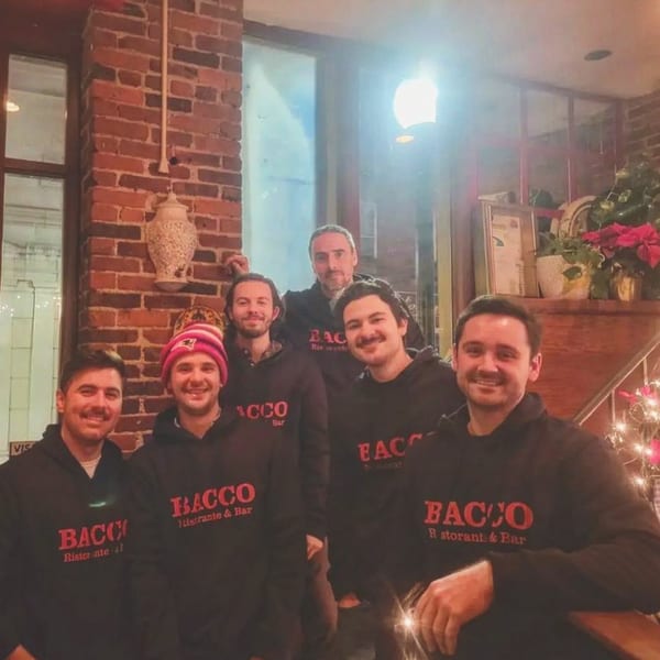 Six smiling Bacco Ristorante & Bar staff members in black hoodies pose inside the restaurant.