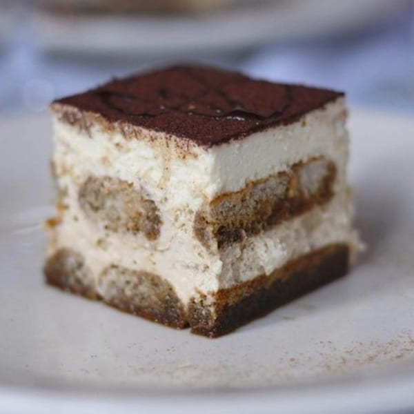 A square slice of Bacco Ristorante's tiramisu, layered with cream and ladyfingers, dusted with cocoa.