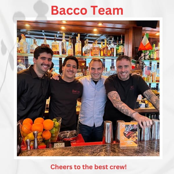 Four smiling Bacco Ristorante & Bar staff members stand behind a well-stocked bar with fresh fruit.