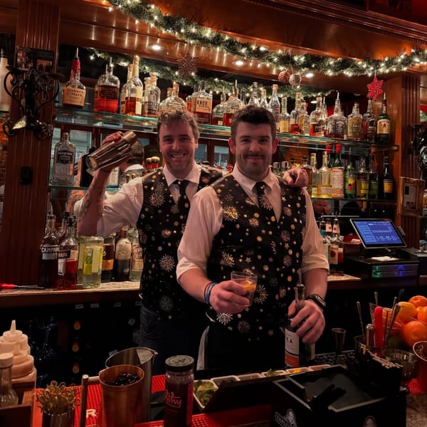 Two smiling Bacco Ristorante & Bar bartenders in festive vests behind a bar with liquor bottles.