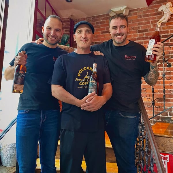 Three smiling men, two wearing Bacco Ristorante & Bar shirts, holding bottles of Copper & Cask.