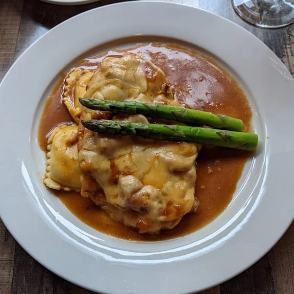 Bacco Ristorante's ravioli dish, topped with melted cheese, rich brown sauce, and two asparagus spears.