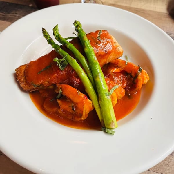 Salmon and shrimp in a rich red sauce, garnished with fresh asparagus on a white plate.