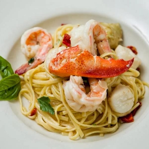 Linguine pasta with lobster, shrimp, and scallops, garnished with basil and parsley.