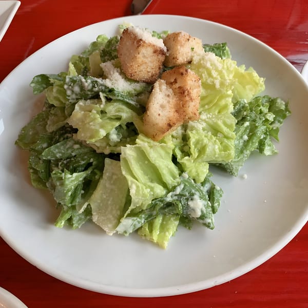 A close-up of a Caesar salad with crisp romaine lettuce, creamy dressing, croutons, and grated cheese.