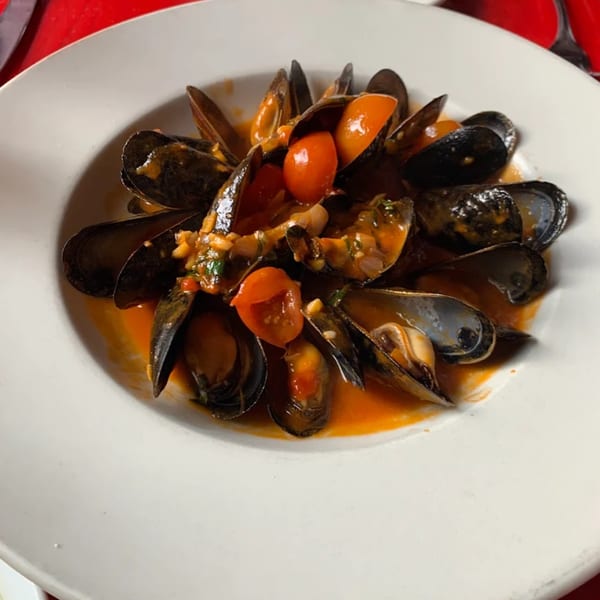 Steamed mussels in a rich red sauce with cherry tomatoes, served in a white bowl.